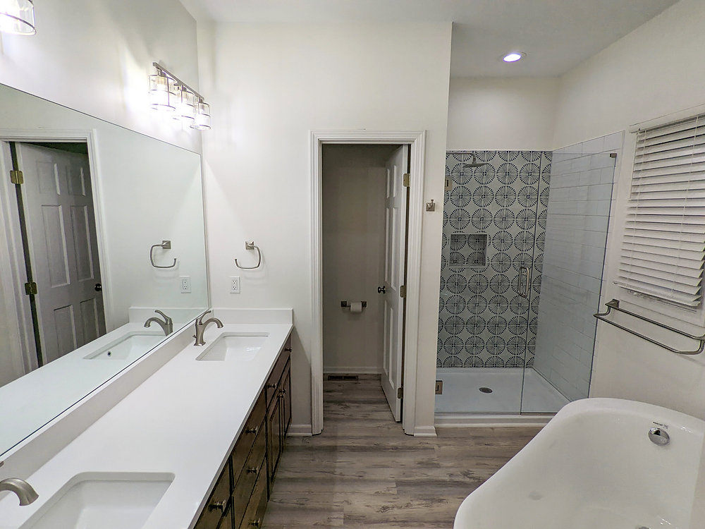 Lee's Summit master bathroom remodel featuring a freestanding tub, tile shower with glass shower door and tile accent wall, LVP flooring, custom walnut vanity and updated brushed nickel fixtures.