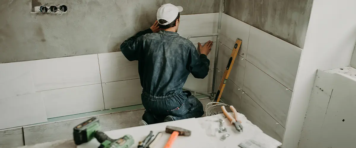 Construction worker installing ceramic tiles on a wall during bathroom remodeling in Raymore.