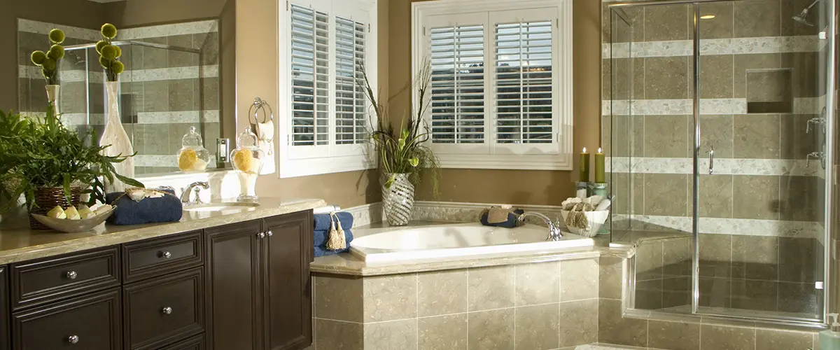 Luxurious bathroom featuring a corner bathtub, large mirror, dark wood vanity, glass-enclosed shower, and decorative plants