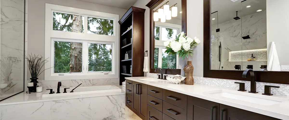 Luxurious bathroom in Raymore, with dark wood cabinets, marble flooring, large mirror, and bathtub with a view of outdoor greenery