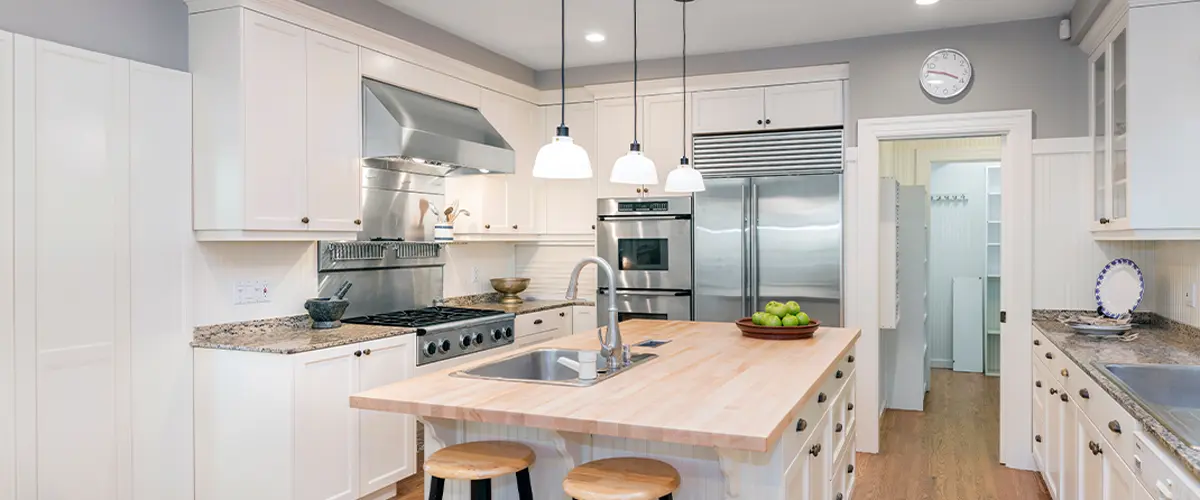 Modern kitchen remodeling in Raymore, with white cabinets, stainless steel appliances, butcher block island, and hardwood floors.