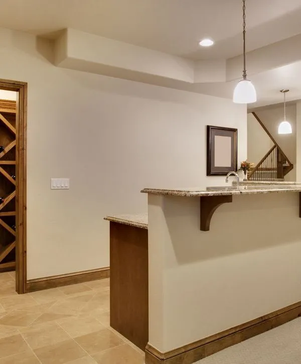 A remodeled basement with a small granite-topped bar, pendant lighting, and a neutral color scheme, offering a sophisticated and functional space for entertaining