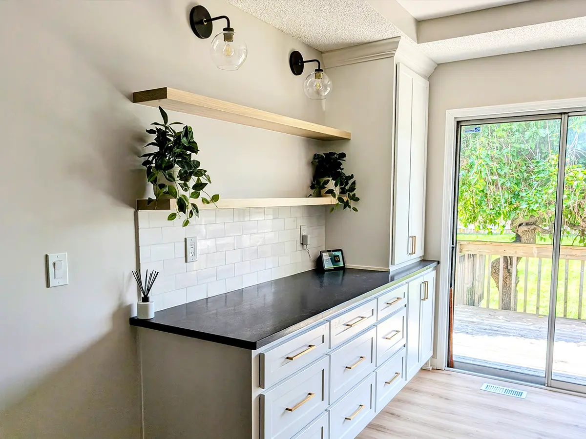 Modern kitchen with white cabinets, black countertop, open shelving, and subway tile backsplash, overlooking patio.