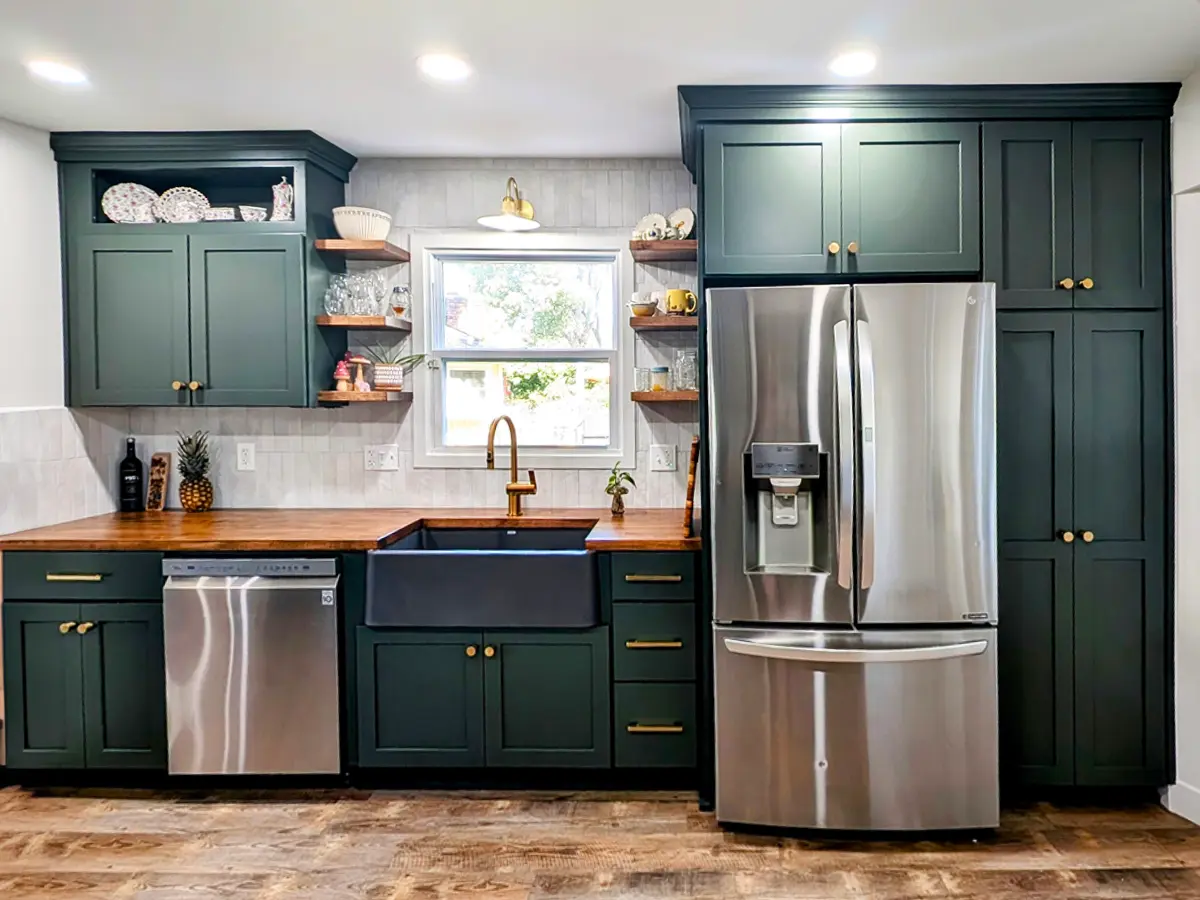 Stylish modern kitchen with green cabinets, farmhouse sink, and stainless steel appliances after remodel.