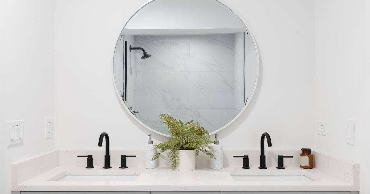 Minimalist bathroom with a white double vanity, black faucets, and a large round mirror