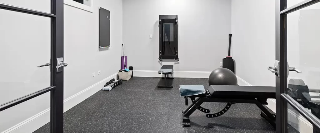 Home gym in a finished basement with rubber flooring, fitness equipment, and natural lighting, highlighting functional home design.